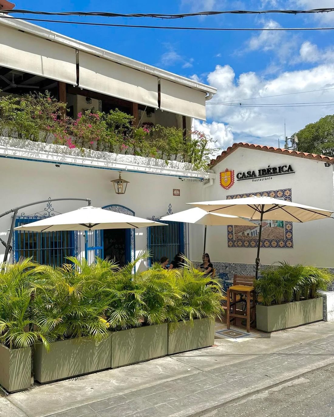 Fachada blanca de Casa Ibérica con su terraza y sombrillas en la Calle La Paz